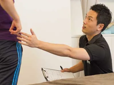 記録用紙を手に身体の状態を確認するトレーナー